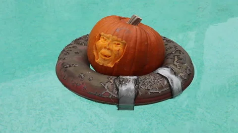 A face carved pumpkin Jack-o-lantern Drifting on a decayed life ring in a pool Stock Footage 158335395