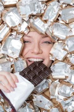 The face of a Caucasian woman surrounded by candy wrappers. The girl eats a bar Stock Photos