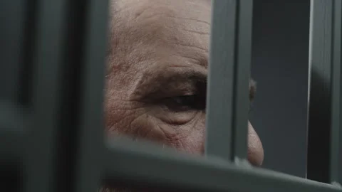 Face close up of angry elderly prisoner standing behind metal bars Stock Footage 245792119
