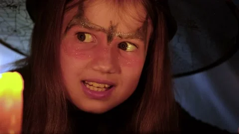 Face of crazy little witch reading spells at Halloween night by candlelight Stock Footage 214223624