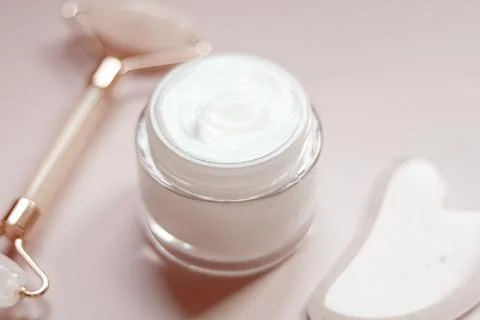 Face cream jar with jade roller and gua sha stone on a light pink backgroun.. Stock Photos