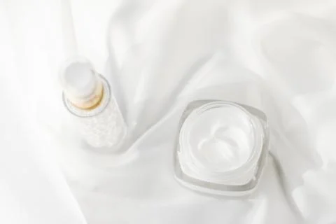 Face cream moisturizer jar and serum gel on white silk, skin care lotion and  Stock Photos