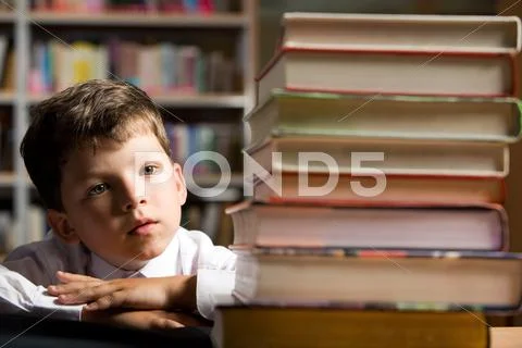 Face of diligent schoolboy looking at stack of books in the library Stock Photos