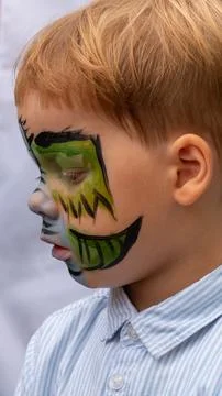 The face of a fair-haired boy close-up with green paint on his face. Stock Photos