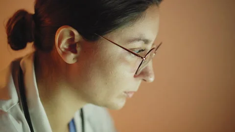 Face of a female doctor working on a computer. Dark scene, she is illuminated Stock Footage 148349162
