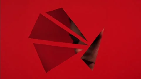 Face of girl appears in triangular holes of red paper background. Stock Footage 86533610
