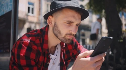 Face handsome young man in the hat uses phone sitting in city blurred background Stock Footage 92071860