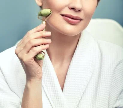 Face jade roller. Cropped face of an adult woman with green jade roller for a Fotos Stock