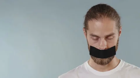 Face man looking at camera serious and tearing tape from her mouth on grey Stock Footage 133639810