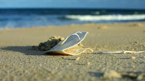 Face Mask Discarded on the Sand at the Beach, Ocean Waves Background Stock Footage 258295954