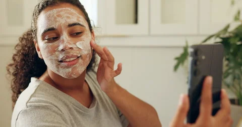 Face mask, phone and tutorial with woman in bathroom of home for cleansing or 動画素材 330588135