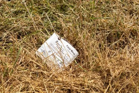 Face mask plastic package left discarded in the grass at the side of the road Stock Photos