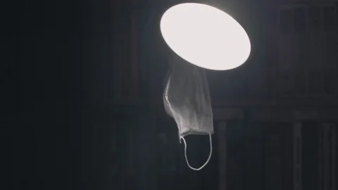 A face mask of the virus hangs on a lamp in a dark room and someone takes it Stock Footage 128281189