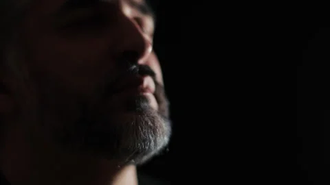 Face of a middle-aged man with a gray beard close-up on a dark background. Video stock 255659647