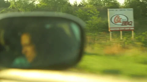 Face in rearview side car mirror driving highway billboard barn sunrise sunset Stock Footage 39787565