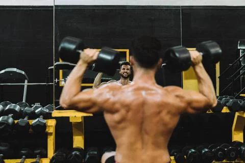 Face reflected in a mirror of a man exercising with dumbbells in a gym Stock Photos