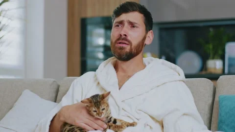 Face sensitive man with cat watching TV. Sitting on sofa cry sad at home Stock Footage 143713239