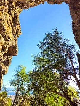 Face-Shaped Cave Opening Framing Native Trees and Blue Sky, Patagonia Foto stock