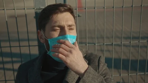 Face sick man wearing Protective Face Mask sitting near fence border sneeze Stock Footage 126617788