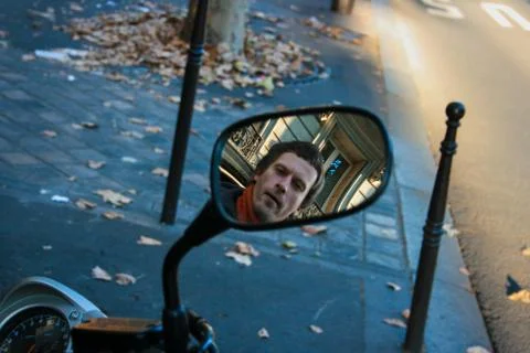 The face of a young man is reflected in the rear view mirror of a moped Stock Photos