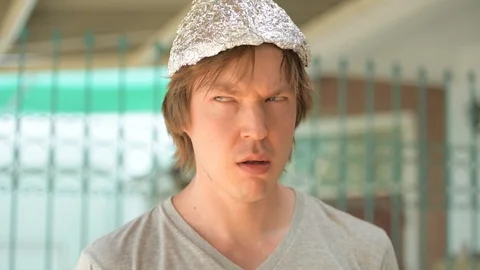 Face of young man with tinfoil hat thinking and looking around outdoors 動画素材 118665148