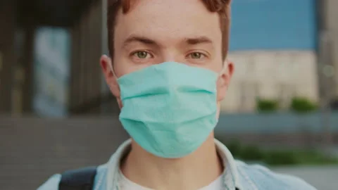 Face young student man with green eyes in a mask look at camera hold books Stock Footage 142048969