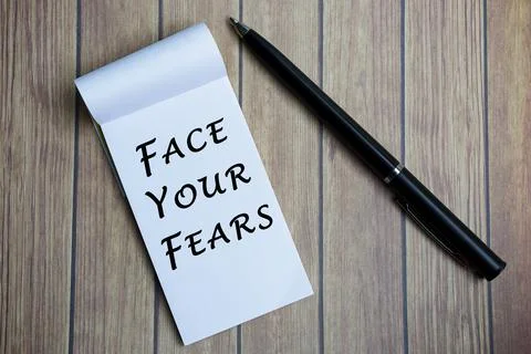 Face your fears text on notepad with a pen on a wooden desk. Stock Photos