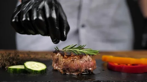 Faceless chef garnishes beef steak with rosemary sprig Stock Footage 240010165
