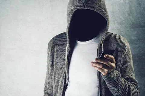 Faceless hooded person using mobile phone, identity theft concept. Stock Photos