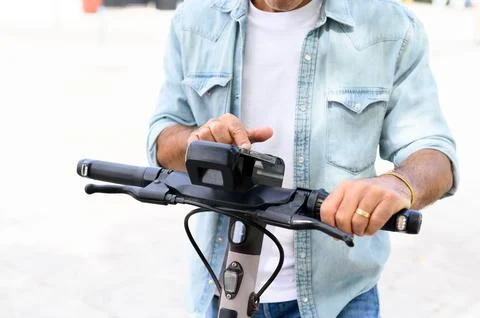 Faceless man browsing smartphone while riding electric scooter on street Stock Photos