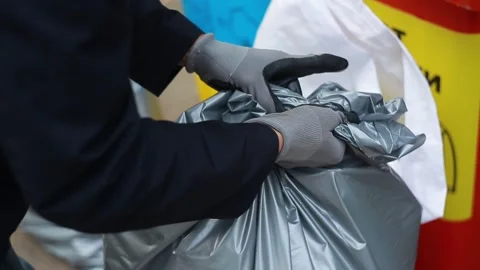 Faceless man in gloves and jacket tying a knot on a gray waste disposal bag Stock Footage 246886025