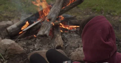 Faceless Man In Hood Sitting By The Fire Outdoors Close-up. Unrecognizable Stock Footage 139612595