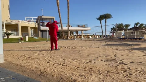 Faceless man in the red suit is raking sand on the beach. Sand leveling on the Stock Footage 169760125