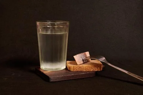 Faceted glass of vodka, rye bread and herring on a fork on a wooden stand Stock Photos