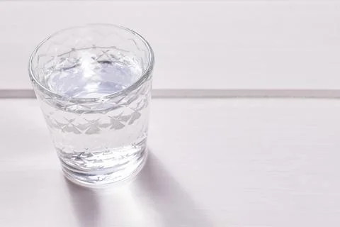 A faceted shot glass of vodka on a white wooden background. Stock Photos