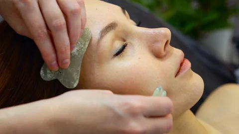 Facial massage master uses gua sha stones. Close-up of client's face, young girl Stock Footage 128071061