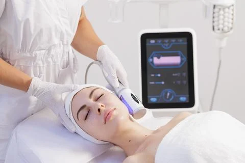 Facial microvibration therapy with LED roller device in clean clinic Stock Photos