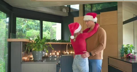 Facing each other, diverse couple hugging under string lights wearing Santa hats Stock Footage 337704910