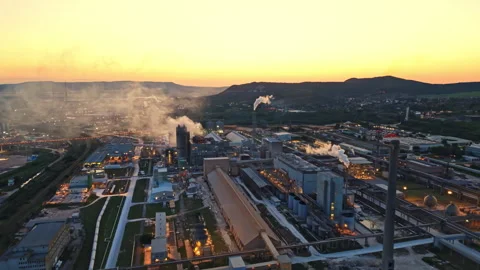 Factory area with smoke and lights during sunset near hills in the background Stock Footage 343574248