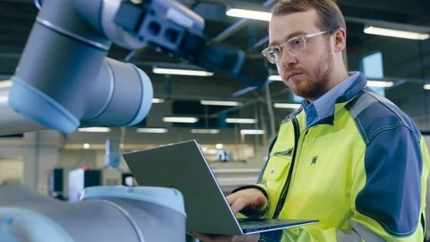 At the Factory: Automation Engineer Uses Laptop for Programming Robotic Arm. Stock Footage 93692897