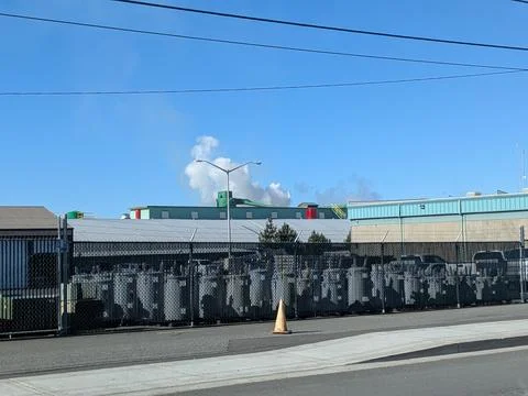 A factory complex with red and green accents releases a plume of white Fotos Stock