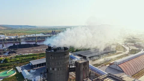 Factory emits smoke above landscape with industrial buildings and machinery in Stock Footage 340946494