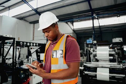 Factory employee checking portable device while examining machinery in industry Stock Photos