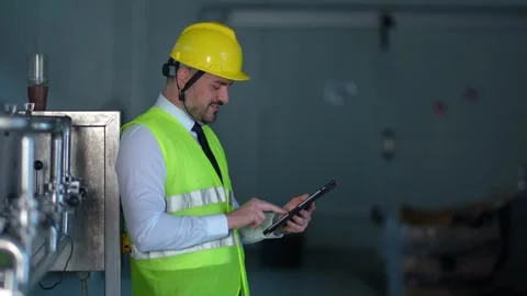 Factory engineer checks a tablet beside stainless steel equipment Stock Footage 348974569