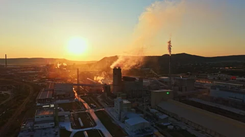 Factory operations at sunset with smoke rising against a mountain backdrop in Stock Footage 341027810