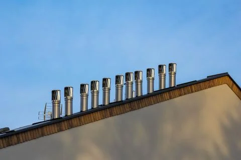 Factory rooftop with multiple metal chimneys under clear blue sky Stock Photos