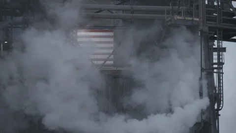 Factory smoke drifting past American flag on factory exterior Stock Footage 89945306