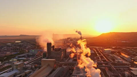 Factory stands under the sunset with smoke rising and orange sky creating a Stock Footage 340945236