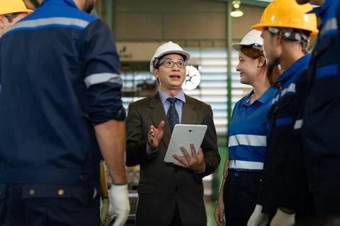 A factory supervisor speaks with industrial workers wearing protective helm.. Stock Photos