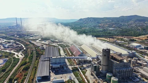 Factory in a valley with smoke rising during daytime hours showcasing industrial Stock Footage 341096072